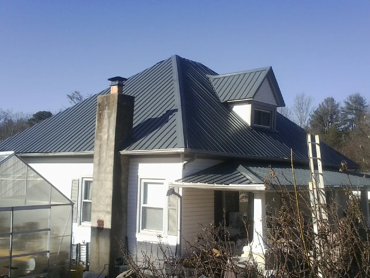 Dark blue standing seam metal roof on a white farmhouse with dormer — Slate & Tile Roof Repair by Roofing Brothers in Leavenworth
