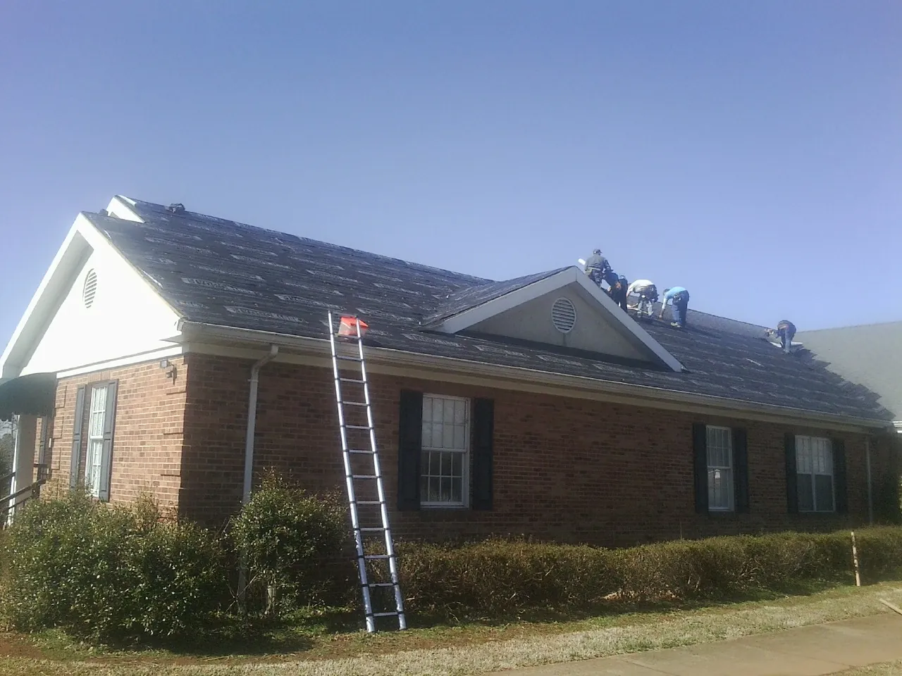 Crew tearing shingles off a brick ranch roof with a ladder set — Metal Roof Repair work by our crew in Leavenworth