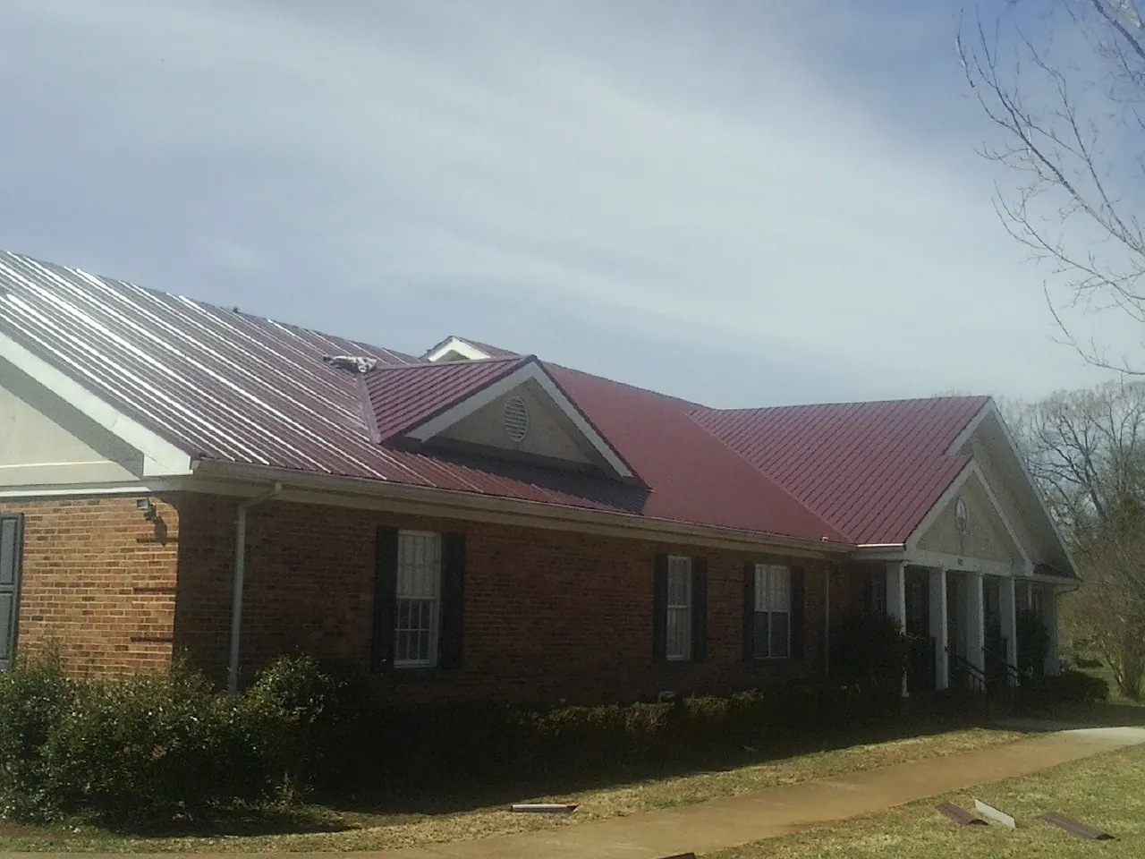 Red metal roof with gabled entries on a long brick building, from a Hail Damage Roof Repair job in Leavenworth