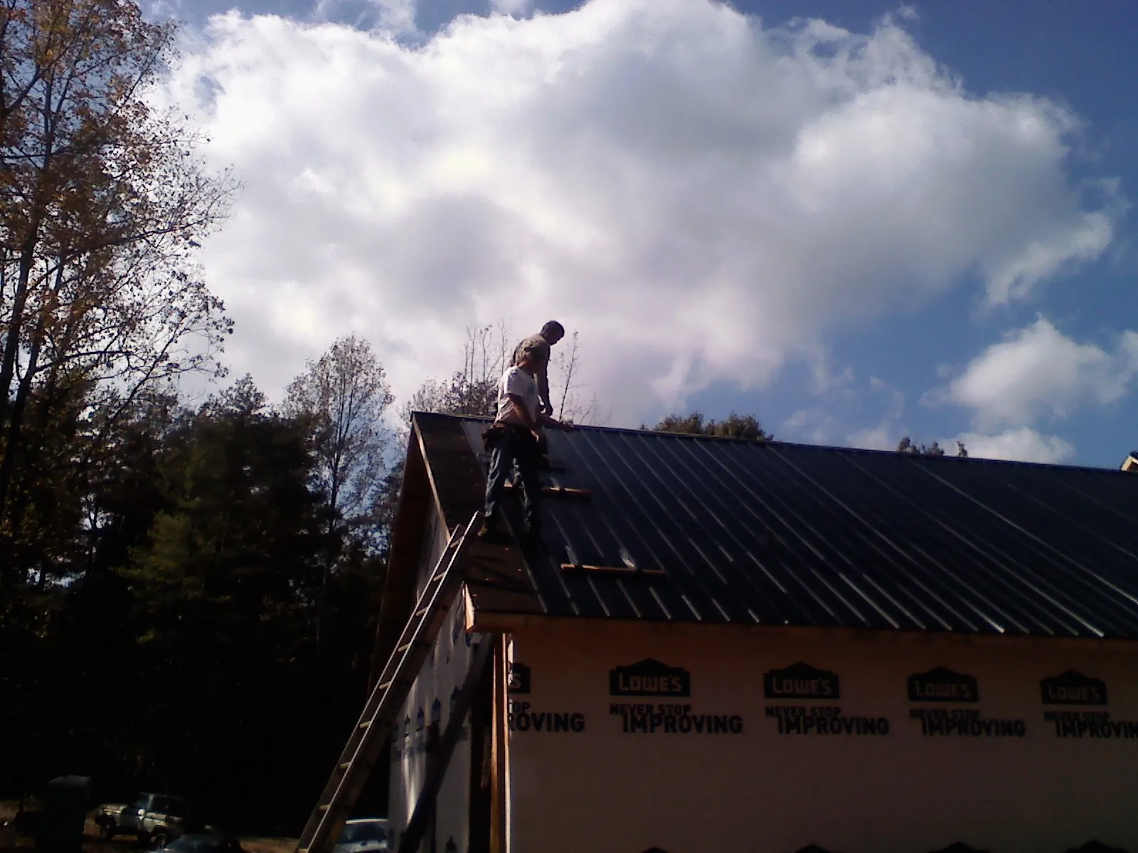 Roofer fastening dark metal panels high against a cloudy sky, from a Roof Inspection job in Leavenworth