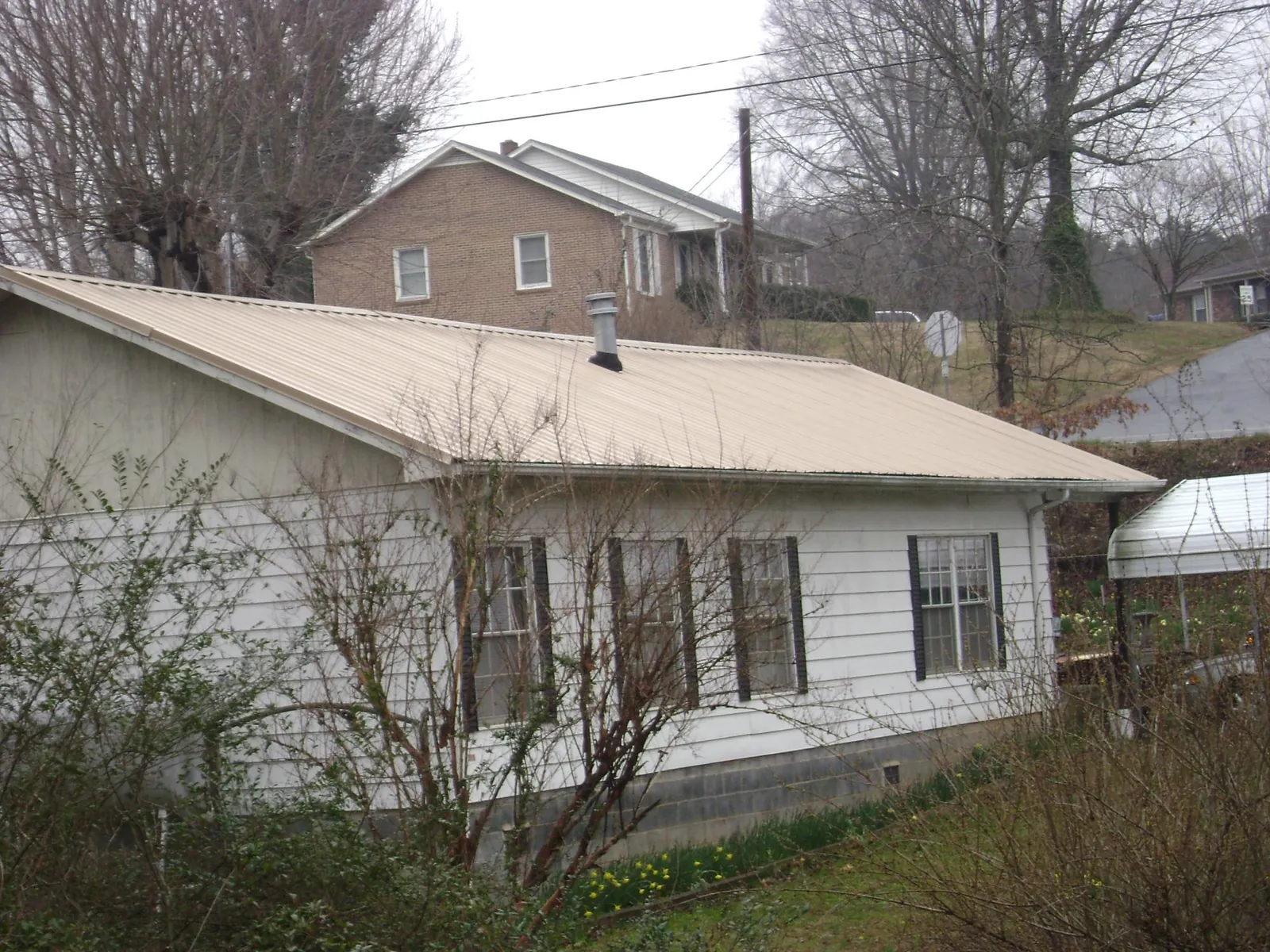 Tan metal roof on a white sided house set into a hillside — Commercial Roofing by Roofing Brothers in Leavenworth